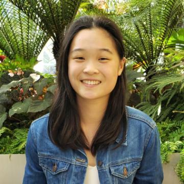A person smiling with greenery in the background, wearing a denim jacket.